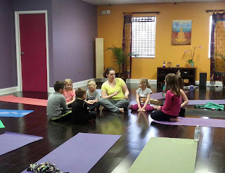 Children and an instructor sitting in a circle on yoga mats in a studio