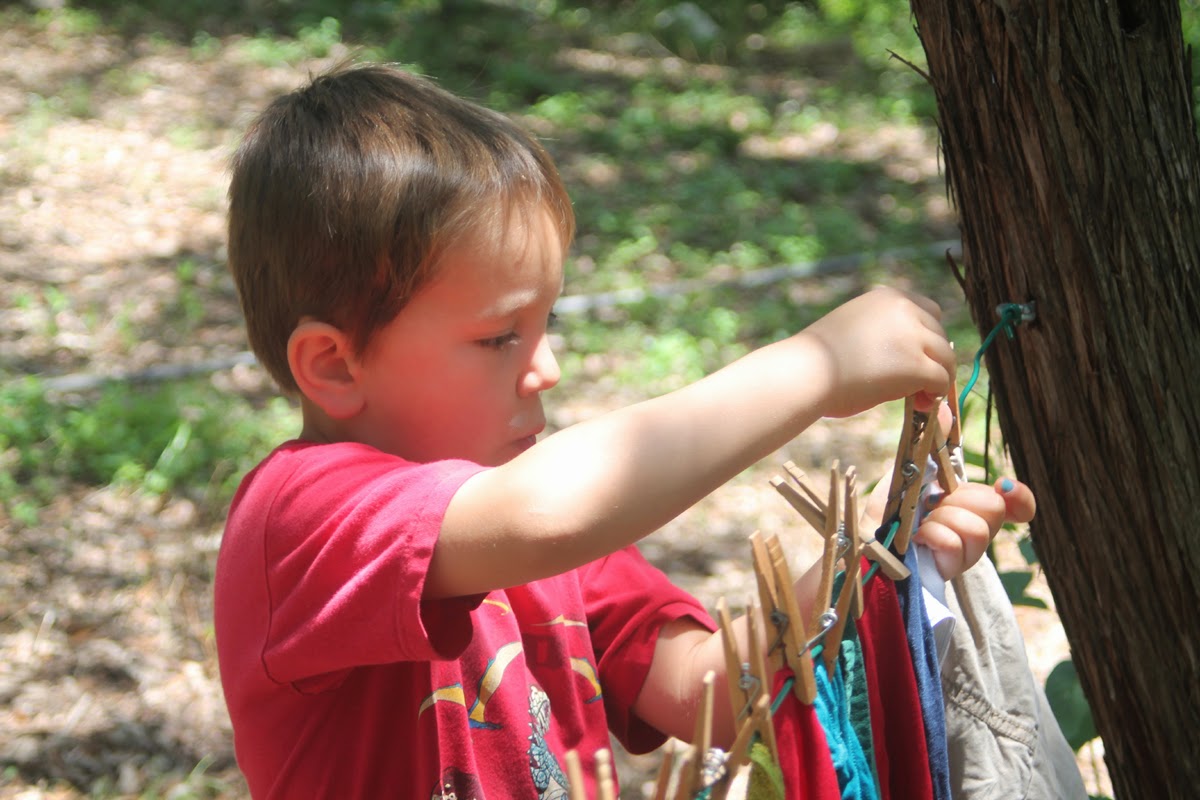 Boy hanging washed clothes on a clothesline with clothespins outdoors