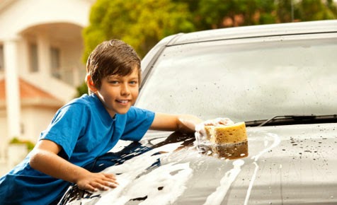 Smiling boy washing a car windshield with a yellow sponge