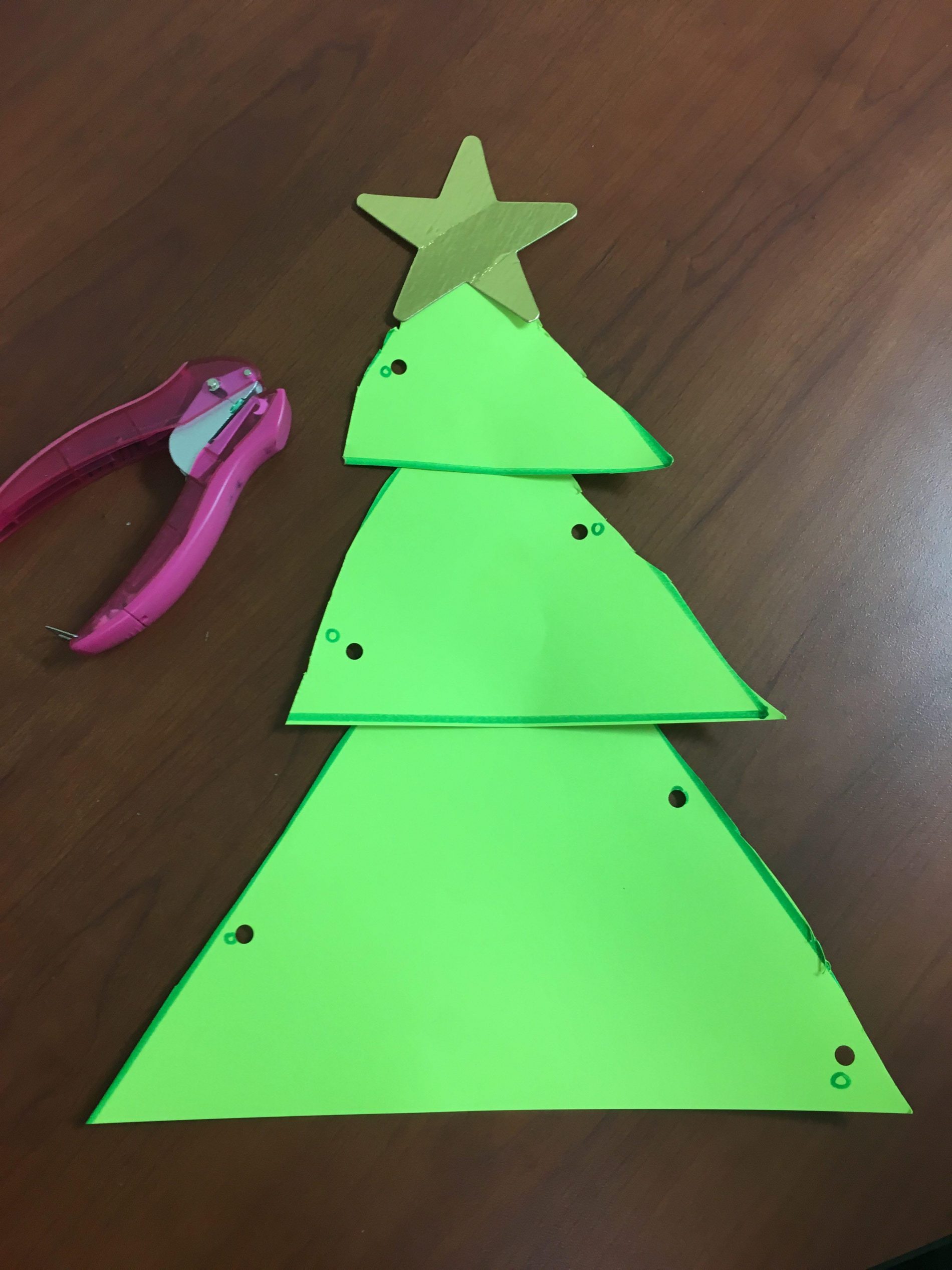 Green paper Christmas tree with a star and punched holes along the sides and a hole punch beside it