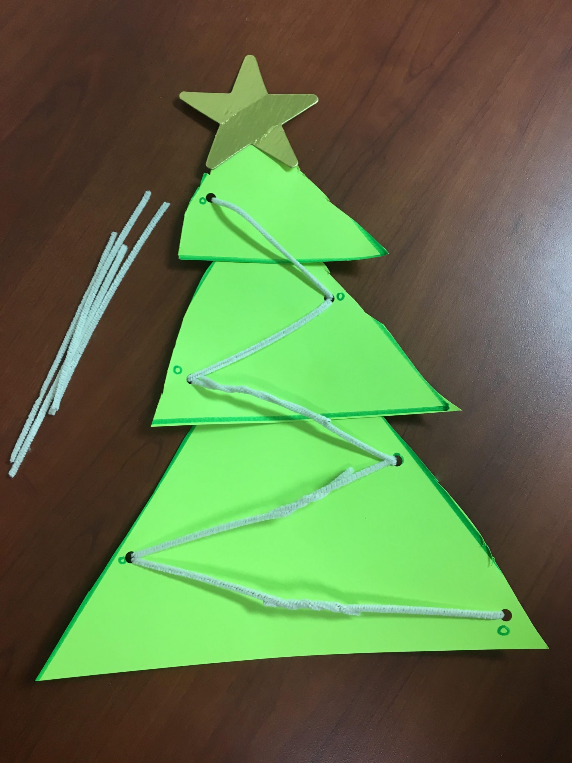 Green paper Christmas tree with white yarn laced back and forth through the holes