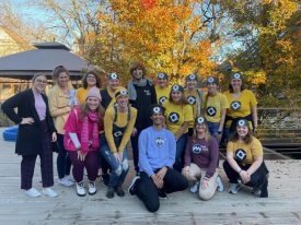 Large group of staff in matching yellow costumes with goggles posing outdoors among autumn trees