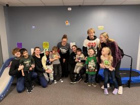 Group of staff and children posing together in a therapy room with a mini trampoline