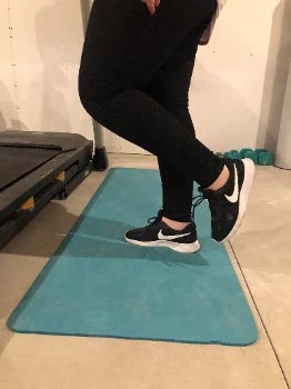 Person standing on one leg on a teal mat with the other foot lifted, demonstrating a flamingo stand