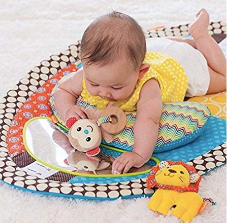 Baby lying on her tummy on a colorful tummy time mat holding a monkey toy
