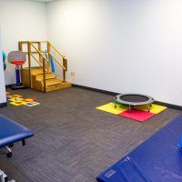 Therapy room with a mini trampoline, blue mats, colored floor squares and a staircase