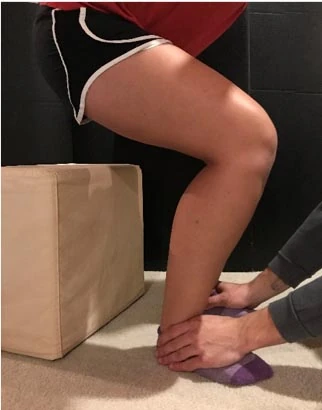 Child's lower leg and foot on the floor while an adult's hands hold the ankle beside a box