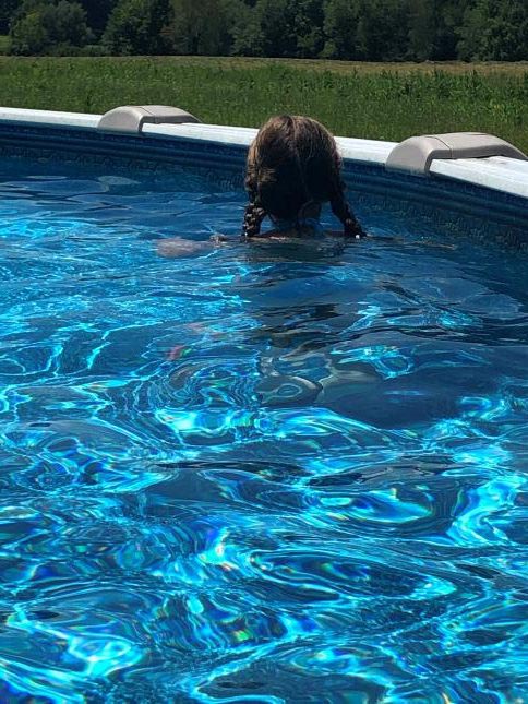 Girl standing in a backyard pool facing away from the camera